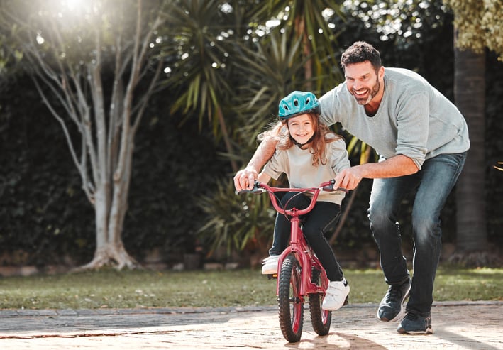 A dad teaches his young child to ride a bike.  She is smiling!  Investment vs. speculation