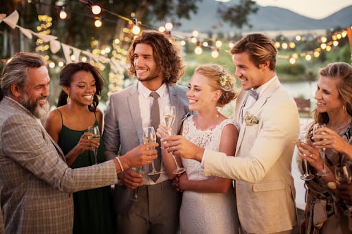 A wedding party toasts a bride and groom at an outdoor reception. Newlywed couples should learn about the marriage tax penalty and how to plan for it.