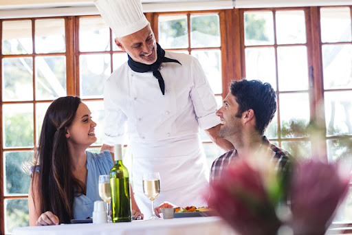 A restaurant owner and chef greets diners in his restaurant. Working with an accountant on restaurant industry best practices helps chefs like this run their business better.