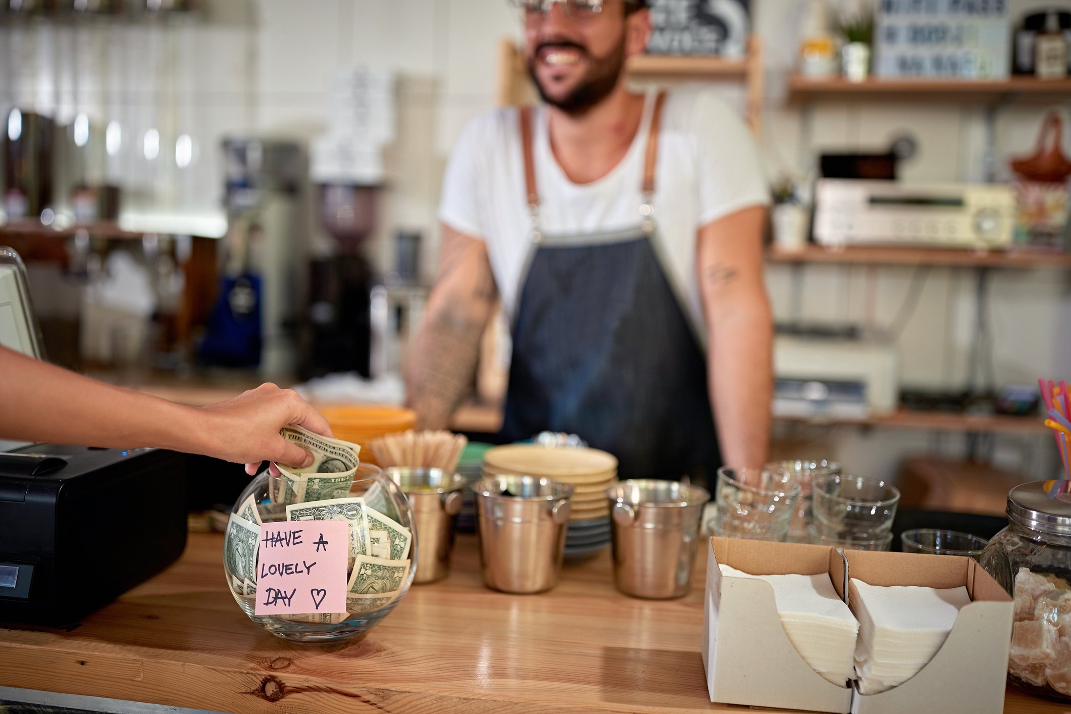 Coffee shop patron giving a tip in a jar. Employee smiling.  