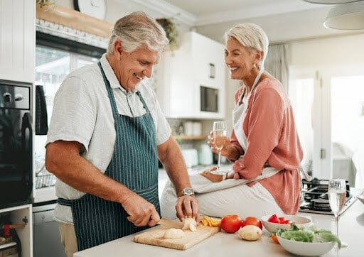 Happy senior couple, cooking in the kitchen as they enjoy retirement. Homeowners considering selling their primary residence should consider maximizing their Section 121 exclusion.