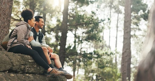 Understanding the impact of economic trends can help investors make thoughtful and strategic investment decisions. A couple relaxes in the forest, sitting on a fallen tree trunk.