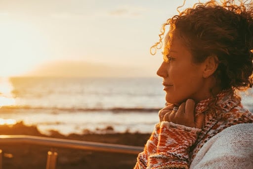 A woman in profile looks out at the ocean during sunset. Getting divorced requires you to revisit financial and insurance plans