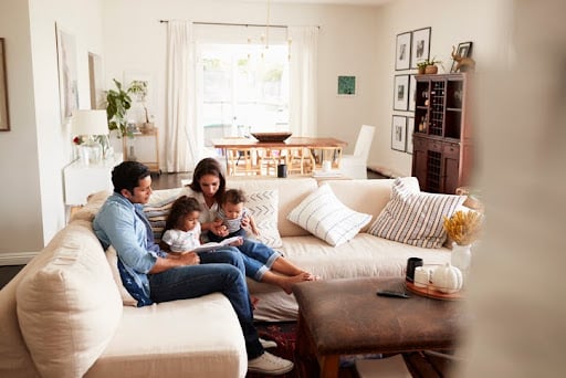 Young family sitting on sofa reading a book together in the living room. Investment planning.