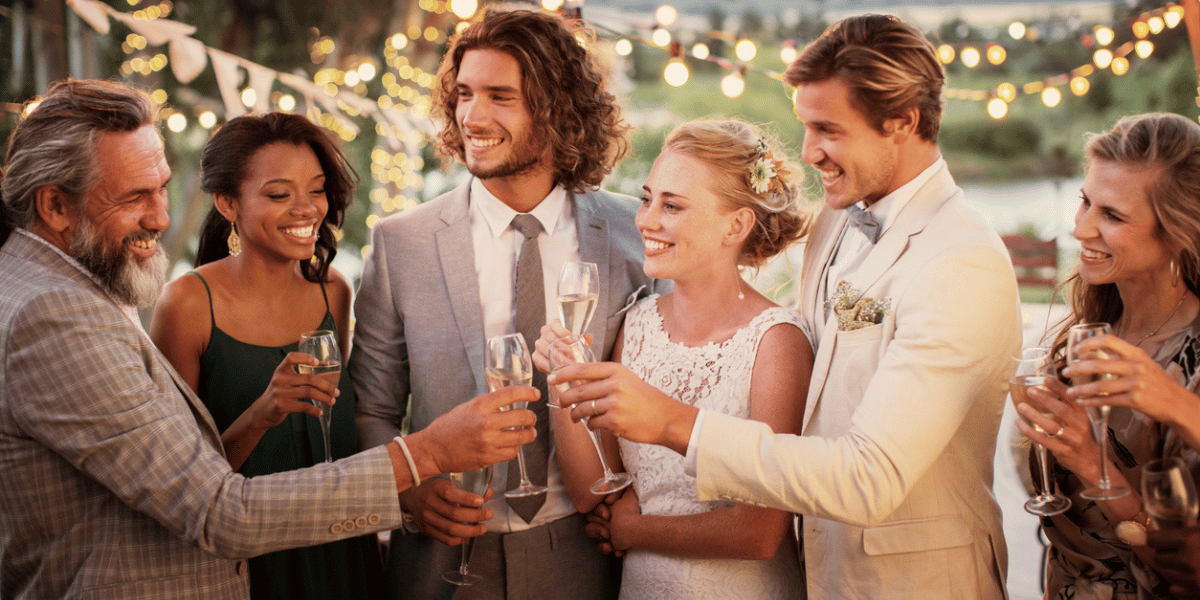 A wedding party toasts a bride and groom at an outdoor reception. Newlywed couples should learn about the marriage tax penalty and how to plan for it.