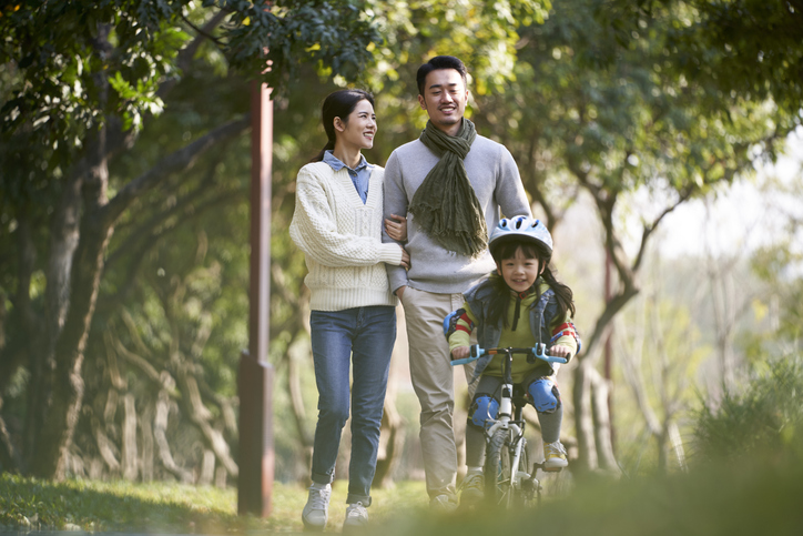 A mother and father smile and walk behind a young child learning to ride a bicycle. Families, business and individuals may benefit from the 2024 Massachusetts tax relief law.
