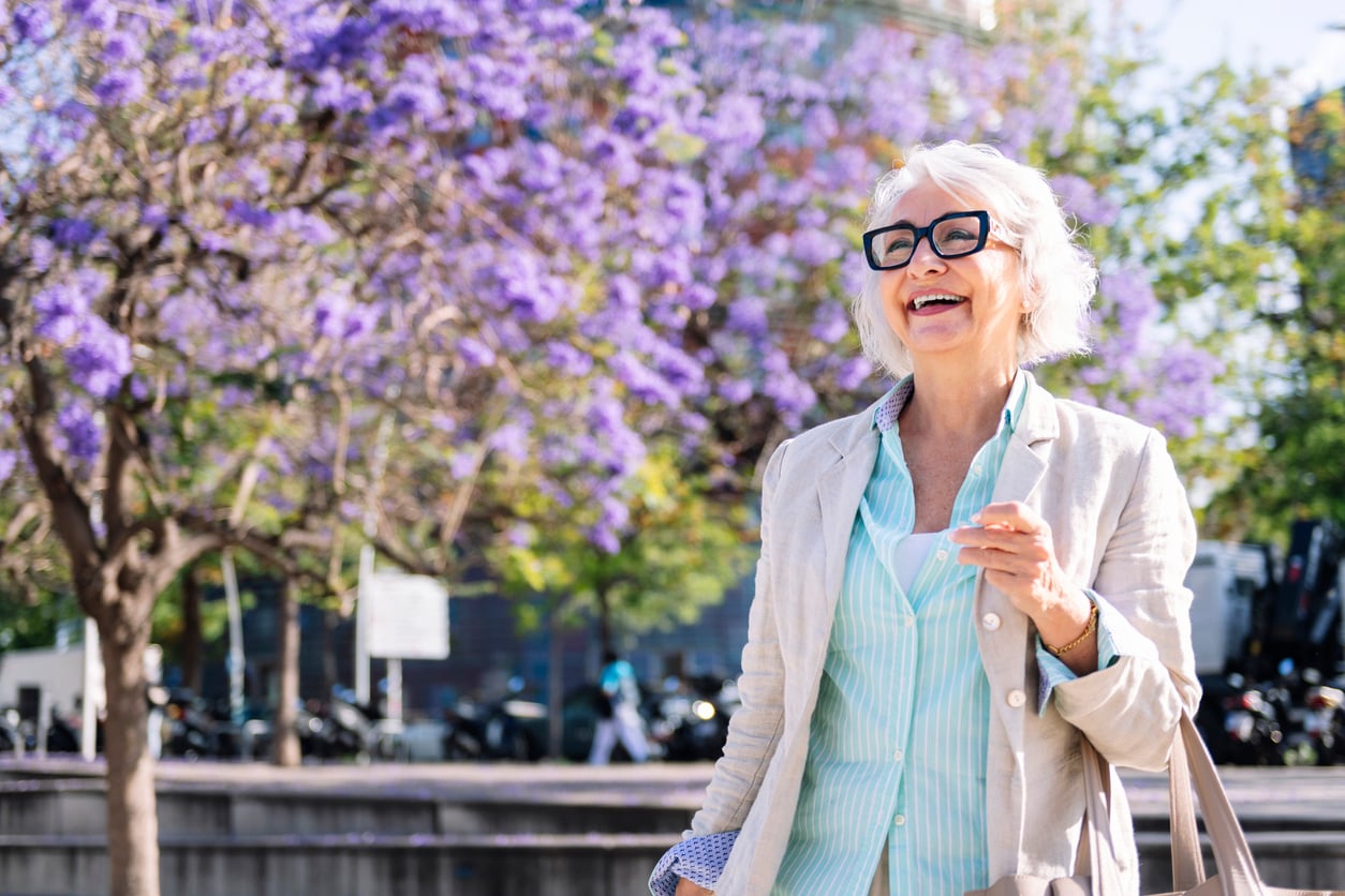 woman around age 65 taking a walk under blossomed trees 